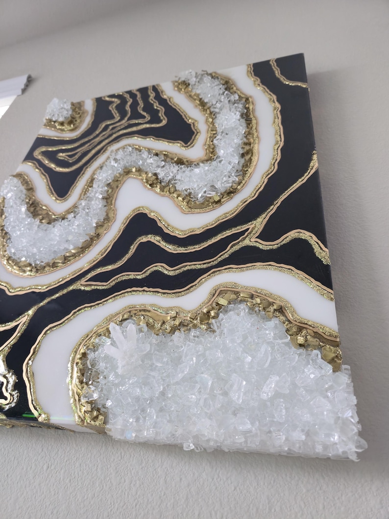 May include: Abstract wall art with a geode design. The artwork features black, white, and gold colours, with clear crystal accents. The design resembles natural stone formations.