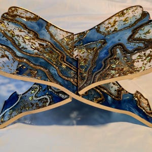 May include: A decorative book stand with a unique design. The stand features a blue and white marbled pattern with gold accents. The stand is made of a sturdy material and is designed to hold books. The stand is approximately 12 inches wide.