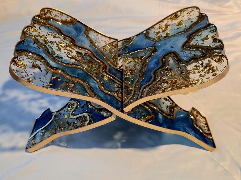 May include: A decorative book stand with a unique design. The stand features a blue and white marbled pattern with gold accents. The stand is made of a sturdy material and is designed to hold books. The stand is approximately 12 inches wide.