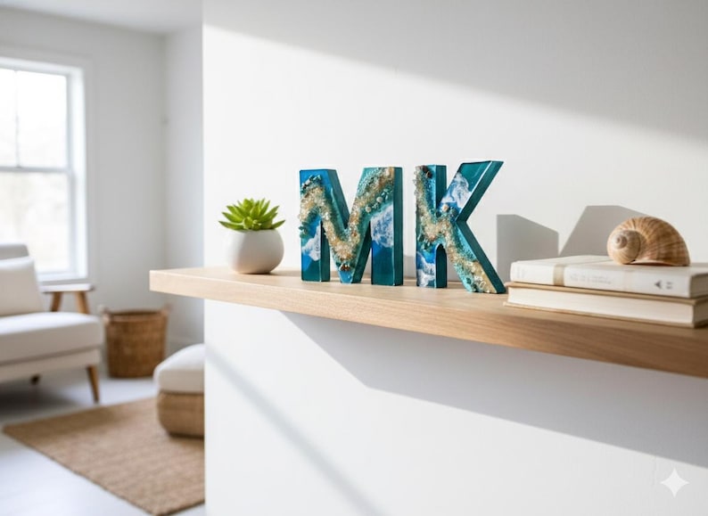 Może przedstawiać: Ozdobne drewniane litery z napisem "MK" z niebieskim i złotym wzorem z żywicy, wystawione na drewnianej p&oacute;łce. Mały sukulent w białej doniczce, muszla i książki r&oacute;wnież znajdują się na p&oacute;łce.