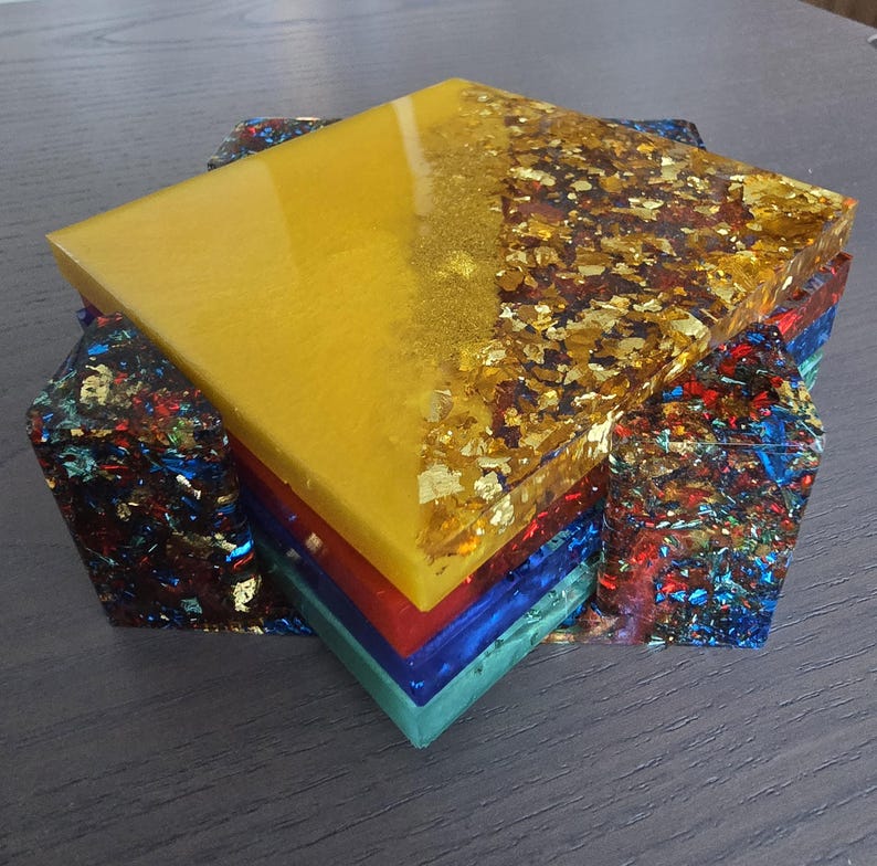 Pode incluir: Um conjunto de bases de resina coloridas. A base superior &eacute; amarela com detalhes em folha de ouro. Abaixo, camadas vermelhas, azuis e turquesas. As laterais s&atilde;o feitas de resina com flocos coloridos.