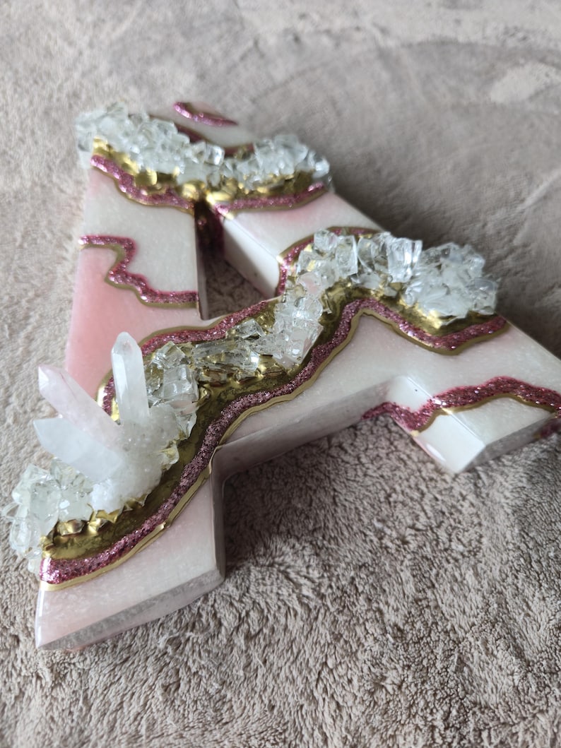 May include: A decorative letter "A" with a pink and white marbled design, accented with gold glitter and clear crystal clusters. The letter is a unique, handcrafted piece.