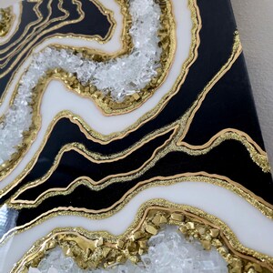 May include: Abstract geode-style artwork. The piece features black and white layers with gold detailing and embedded crystals. The artwork has a glossy finish and a textured appearance, creating a luxurious aesthetic.