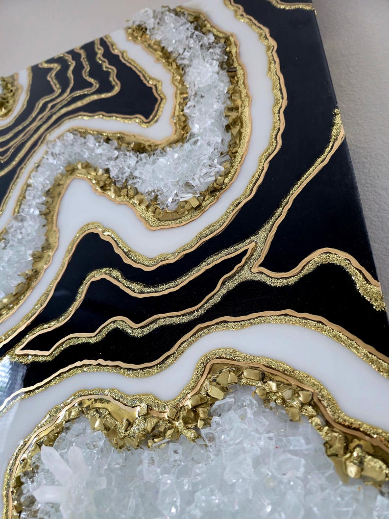May include: Abstract geode-style artwork. The piece features black and white layers with gold detailing and embedded crystals. The artwork has a glossy finish and a textured appearance, creating a luxurious aesthetic.