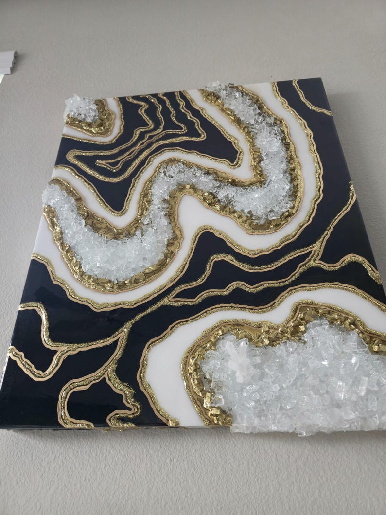May include: Abstract wall art with a geode design. The artwork features a black, white, and gold colour scheme with clear crystal accents. The piece has a glossy finish and is mounted on a wall.