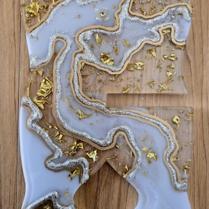 K&ouml;nnte beinhalten: Ein dekorativer Telefonst&auml;nder aus klarem Harz mit einem wei&szlig;en und silbernen Marmormuster. Goldfolie und kleine Perlen sind in den St&auml;nder eingebettet. Der St&auml;nder ist etwa 15 cm hoch und 10 cm breit.