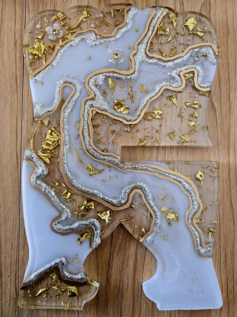 K&ouml;nnte beinhalten: Ein dekorativer Telefonst&auml;nder aus klarem Harz mit einem wei&szlig;en und silbernen Marmormuster. Goldfolie und kleine Perlen sind in den St&auml;nder eingebettet. Der St&auml;nder ist etwa 15 cm hoch und 10 cm breit.