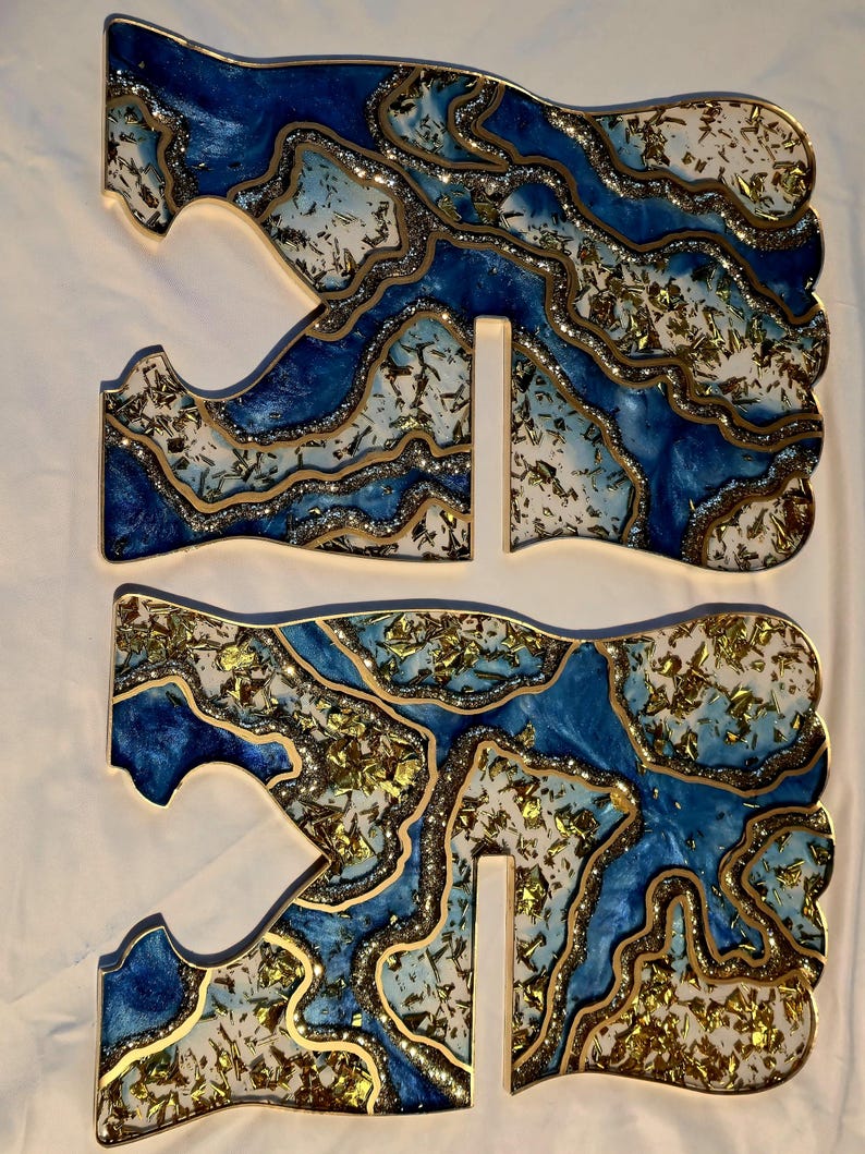 May include: Three-piece set of decorative resin art. The pieces feature a blue, white, and gold design with a glittery, layered effect. The edges are outlined in gold, creating a unique, artistic look. The pieces are designed to stand upright.