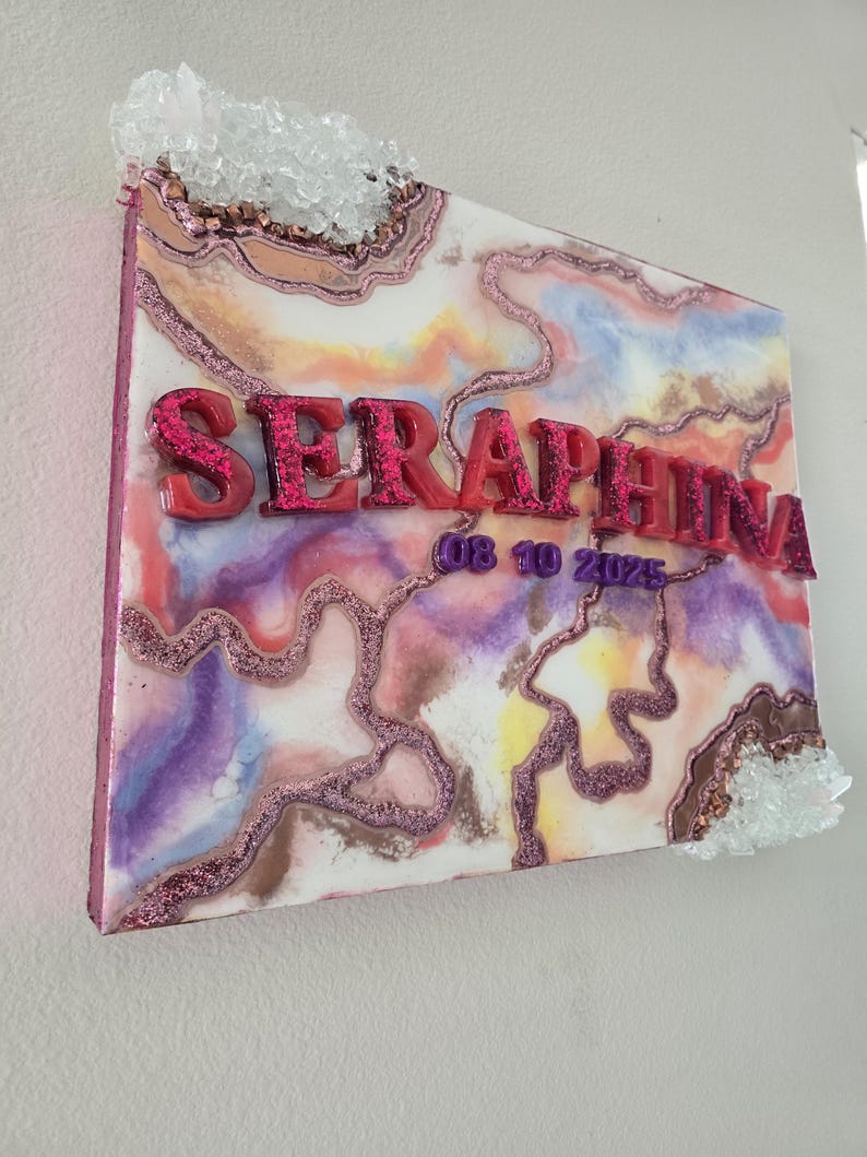 Puede incluir: Una pieza de arte mural decorativa con el nombre "SERAPHINA" en letras rojas con purpurina. La obra presenta un dise&ntilde;o abstracto colorido con tonos rosas, morados y marrones, acentuado con purpurina y adornos de cristal. Tambi&eacute;n es visible la fecha "08 10 2025".