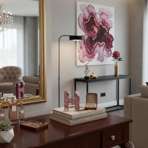 May include: A dark wood vanity table with a gold-framed mirror, featuring decorative items like perfume bottles, a succulent, and a pink letter "H". A painting with pink and gold floral design hangs on the wall.