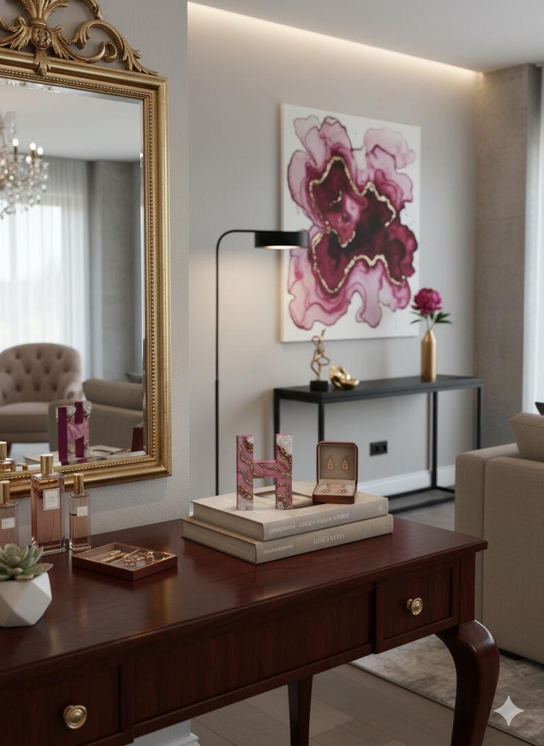 May include: A dark wood vanity table with a gold-framed mirror, featuring decorative items like perfume bottles, a succulent, and a pink letter "H". A painting with pink and gold floral design hangs on the wall.