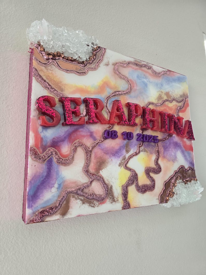 Puede incluir: Una pieza de arte mural decorativa con un dise&ntilde;o abstracto y colorido. La obra presenta el nombre "SERAPHINA" en letras en relieve y brillantes, junto con la fecha "08 10 2025". Racimos de cristales transparentes adornan los bordes superior e inferior.