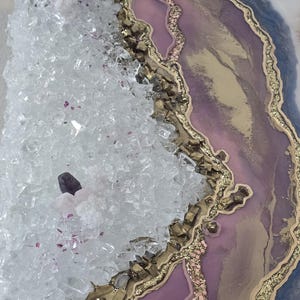 Może przedstawiać: Dekoracyjne dzieło sztuki inspirowane geodami, z krystaliczną strukturą po lewej stronie i warstwowym wzorem po prawej stronie. Dzieło zawiera przezroczyste kryształy, odcienie fioletu, złote akcenty i brokat.