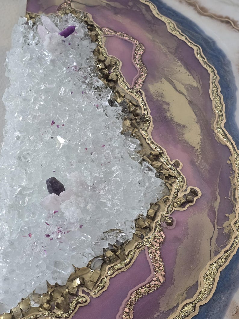 Może przedstawiać: Dekoracyjne dzieło sztuki inspirowane geodami, z krystaliczną strukturą po lewej stronie i warstwowym wzorem po prawej stronie. Dzieło zawiera przezroczyste kryształy, odcienie fioletu, złote akcenty i brokat.