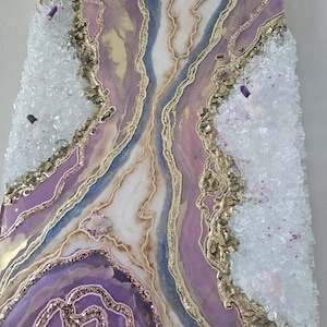 Może przedstawiać: Abstrakcyjna grafika ścienna z motywem geody w odcieniach fioletu, bieli, złota i błękitu. Grafika zawiera kryształowe akcenty i brokat, tworząc teksturowany i dekoracyjny element. Og&oacute;lnym motywem jest naturalna estetyka inspirowana kamieniami szlachetnymi.