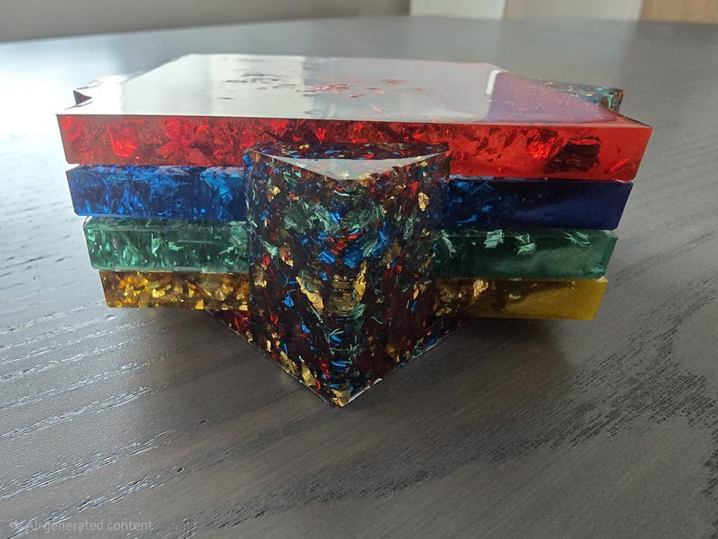Pode incluir: Um conjunto de bases para copos de resina coloridas. As bases para copos s&atilde;o vermelhas, azuis, verdes e amarelas, com uma camada superior transparente. A pe&ccedil;a central &eacute; um prisma triangular multicolorido. Feito com flocos de folha de ouro.
