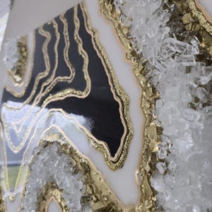 May include: Abstract wall art with a geode design in black, white, and gold. The artwork has a glossy finish and is embellished with clear, crystalline elements along the edges, creating a textured, dimensional effect.