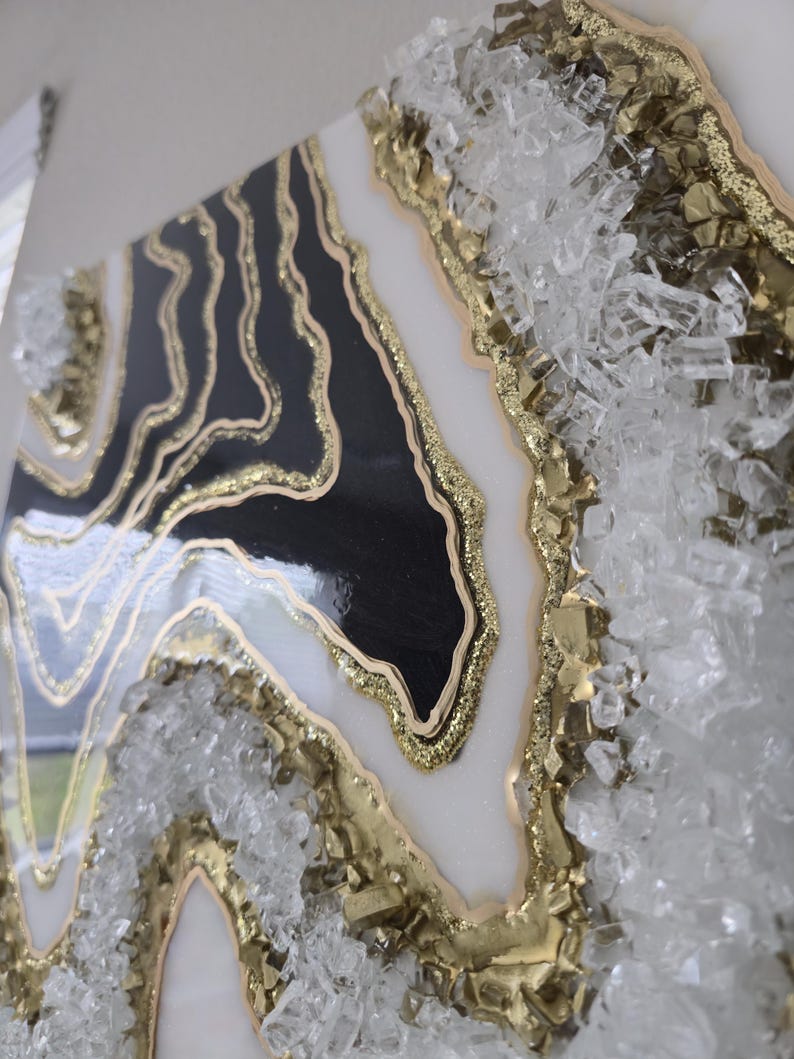 May include: Abstract wall art with a geode design in black, white, and gold. The artwork has a glossy finish and is embellished with clear, crystalline elements along the edges, creating a textured, dimensional effect.