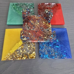 Pode incluir: Um conjunto de bases para copos de resina coloridas. As bases quadradas apresentam v&aacute;rias cores, incluindo verde, vermelho, amarelo e azul. Algumas bases t&ecirc;m detalhes em folha de ouro e glitter, criando um efeito decorativo. As bases s&atilde;o para decora&ccedil;&atilde;o de casa.