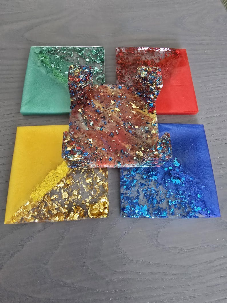 Pode incluir: Um conjunto de bases para copos de resina coloridas. As bases quadradas apresentam v&aacute;rias cores, incluindo verde, vermelho, amarelo e azul. Algumas bases t&ecirc;m detalhes em folha de ouro e glitter, criando um efeito decorativo. As bases s&atilde;o para decora&ccedil;&atilde;o de casa.