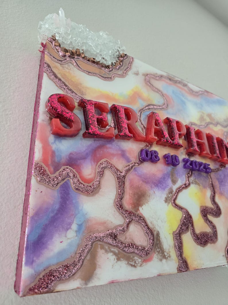 Puede incluir: Una colorida obra de arte abstracta en resina con la palabra "SERAPHINA" en letras rojas con purpurina. La obra presenta una mezcla de tonos rosas, morados, azules y amarillos, detalles con purpurina y un grupo de cristales en la parte superior.