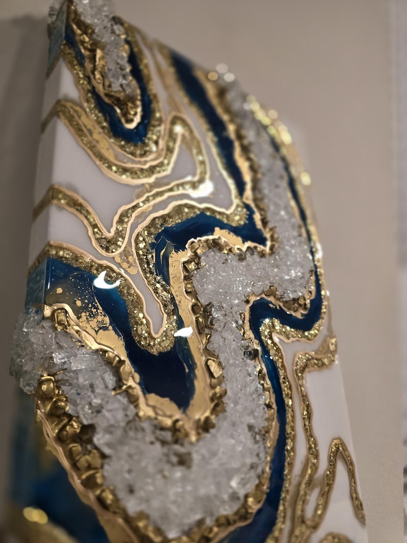 May include: Abstract art piece with a geode design. The artwork features a white base with blue and gold accents. The design incorporates crystal-like elements and gold-colored borders, creating a textured and layered appearance.