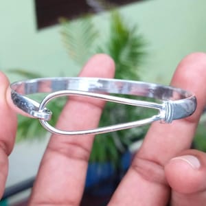 Puede incluir: Un brazalete plateado con cierre de gancho y ojo. El brazalete tiene un diseño redondo y un acabado pulido. El cierre de gancho es una característica clave, que añade un toque distintivo a la joyería.