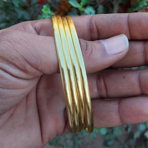 Peut inclure: Quatre bracelets dorés sont tenus dans une main. Les bracelets sont lisses et brillants, reflétant la lumière. Les bijoux sont d'un design simple et élégant, adaptés au quotidien ou aux occasions spéciales.