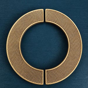 May include: A set of four gold-toned, semi-circular cabinet pulls arranged to form a circle. Each pull has a textured, cross-hatched surface and a smooth, rounded edge. The pulls are set against a dark teal background.