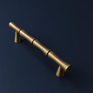 Może przedstawiać: Złoty uchwyt do szafki w stylu bambusowym na ciemnoniebieskim tle. Uchwyt ma cylindryczny kształt z segmentowanymi sekcjami i stożkowymi podporami końcowymi. Odpowiedni do szuflad i szafek.