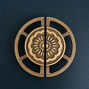 以下が含まれることがあります： アンティーク真鍮製のドアハンドル2つ。各ハンドルは、中央に花柄のデザインがあり、線状のアクセントが付いた円形のフレームで囲まれています。ハンドルは濃い青色の背景に配置されています。