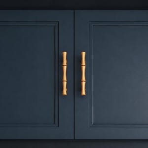 May include: Two navy blue cabinet doors with gold bamboo-style handles. The doors are rectangular with a recessed panel design. The handles are vertical and have a natural bamboo look, adding a touch of elegance to the cabinetry.