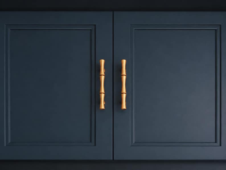 May include: Two navy blue cabinet doors with gold bamboo-style handles. The doors are rectangular with a recessed panel design. The handles are vertical and have a natural bamboo look, adding a touch of elegance to the cabinetry.