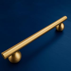 以下が含まれることがあります： 円筒形のバーと球形の端部を備えた、金色のキャビネットプル。 金色の金具は濃い青色の背景に配置されており、金属仕上げとモダンなデザインを際立たせています。 引き出しやキャビネットに適しています。