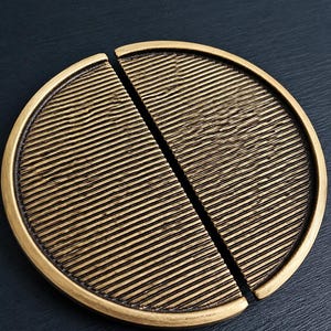 May include: A pair of antique brass cabinet pulls. Each pull is a half-circle with a textured, ridged surface. The pulls are divided by a vertical line, creating a complete circle when joined. The pulls have a warm, golden hue.