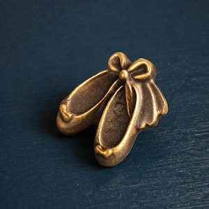 Peut inclure: Une paire de chaussons de ballet de couleur bronze avec des nœuds. Les chaussures, avec leur design détaillé, sont mises en valeur sur un fond bleu foncé. L'image est une prise de vue rapprochée, soulignant les détails.
