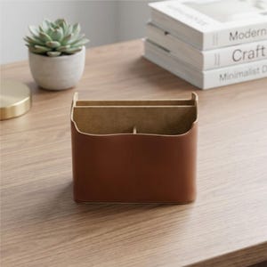 May include: A brown leather desk tidy with three compartments. The organiser sits on a wooden desk next to a small potted succulent and a stack of books titled "Modern", "Craft", and "Minimalist Design".