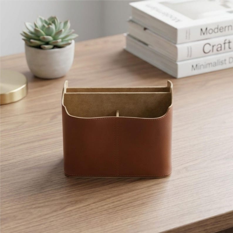 May include: A brown leather desk tidy with three compartments. The organiser sits on a wooden desk next to a small potted succulent and a stack of books titled "Modern", "Craft", and "Minimalist Design".