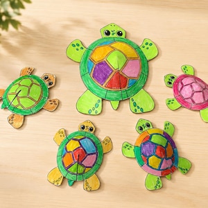 May include: Five paper turtle crafts arranged in a group. The turtles feature colourful, segmented shells in shades of green, yellow, orange, pink, and purple. Each turtle has a distinct head, four flippers, and a raised, three-dimensional shell structure.