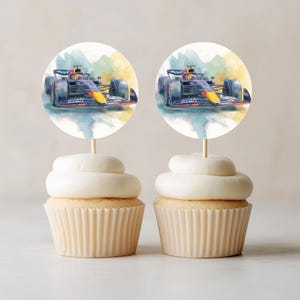 Pode incluir: Dois cupcakes com decorações circulares de papel apresentando uma ilustração em estilo aquarela de um carro de corrida de Fórmula 1 azul-escuro e amarelo. Os topos estão montados em palitos de madeira inseridos na cobertura branca.