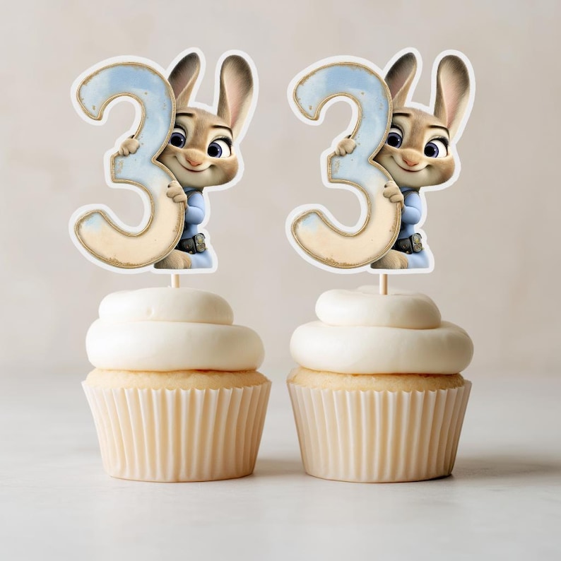 Puede incluir: Dos cupcakes cubiertos con glaseado blanco y un adorno decorativo con el personaje Judy Hopps de Zootopia sosteniendo el n&uacute;mero 3. El n&uacute;mero es azul claro con un borde beige.