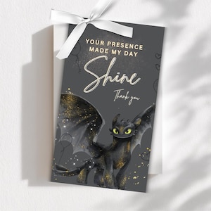 Op de afbeelding: Een donkergrijze kaart met een wit lint toont een zwarte drakenillustratie en de woorden "Your presence made my day Shine Thank you." Gouden glitter accentueert het ontwerp. Een bedankkaart.