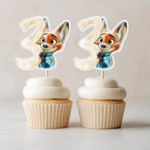 Puede incluir: Dos cupcakes cubiertos con un zorro de dibujos animados sosteniendo el n&uacute;mero 2. El zorro lleva un uniforme azul y tiene pelaje naranja. Los cupcakes tienen glaseado blanco y est&aacute;n en moldes de papel beige. El fondo es de color beige claro.