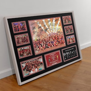 Könnte beinhalten: Gerahmte Collage mit mehreren Fotos eines Teams in Rot, mit Unterschriften und Text. Das zentrale Bild zeigt eine Gruppe von Personen. Der Rahmen ist weiß mit schwarzem Passepartout und roten Akzenten. Der Text "The Champions Wall" ist sichtbar.