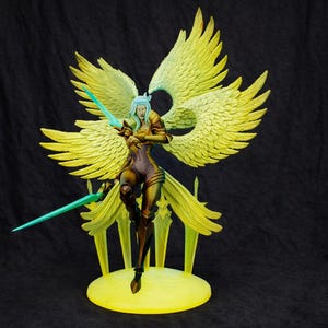 Puede incluir: Figura detallada de un ángel femenino con grandes alas amarillas y una espada verde azulado. La figura lleva un atuendo marrón y morado y se encuentra sobre una base amarilla. El fondo es negro.