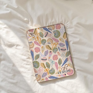 May include: A rectangular case with a seashell design in pastel shades. The pattern includes various seashells, ribbons, and the word "CUSTOM". The case is set against a white background.