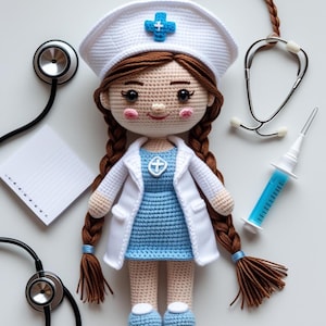 Peut inclure: Poupée infirmière au crochet faite à la main, avec des tresses brunes, portant un chapeau blanc avec une croix bleue, une robe bleue et un manteau blanc. Un stéthoscope, un bloc-notes et une seringue sont placés autour de la poupée. La poupée mesure environ 20 cm de haut.