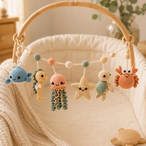 May include: A wooden arch baby gym toy featuring six crocheted sea creatures including a blue whale, a yellow seahorse, a pink jellyfish, a yellow starfish, a green and cream turtle, and an orange crab, all suspended from a white cord.
