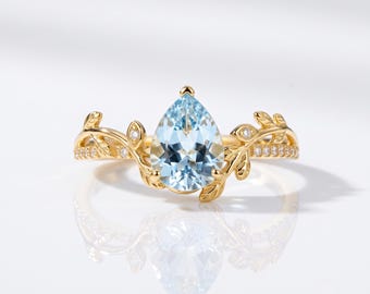 Peut inclure: Une bague en or avec une pierre précieuse bleu clair en forme de poire au centre. L'anneau présente des motifs de feuilles en métal complexes s'étendant depuis le centre, agrémentés de petites pierres claires incrustées sur les côtés.