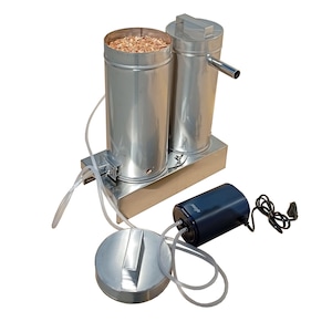 May include: A stainless steel smoker with two cylindrical chambers, one filled with wood chips. A dark blue air pump and a lid are connected with clear tubing. The device is designed for smoking food.